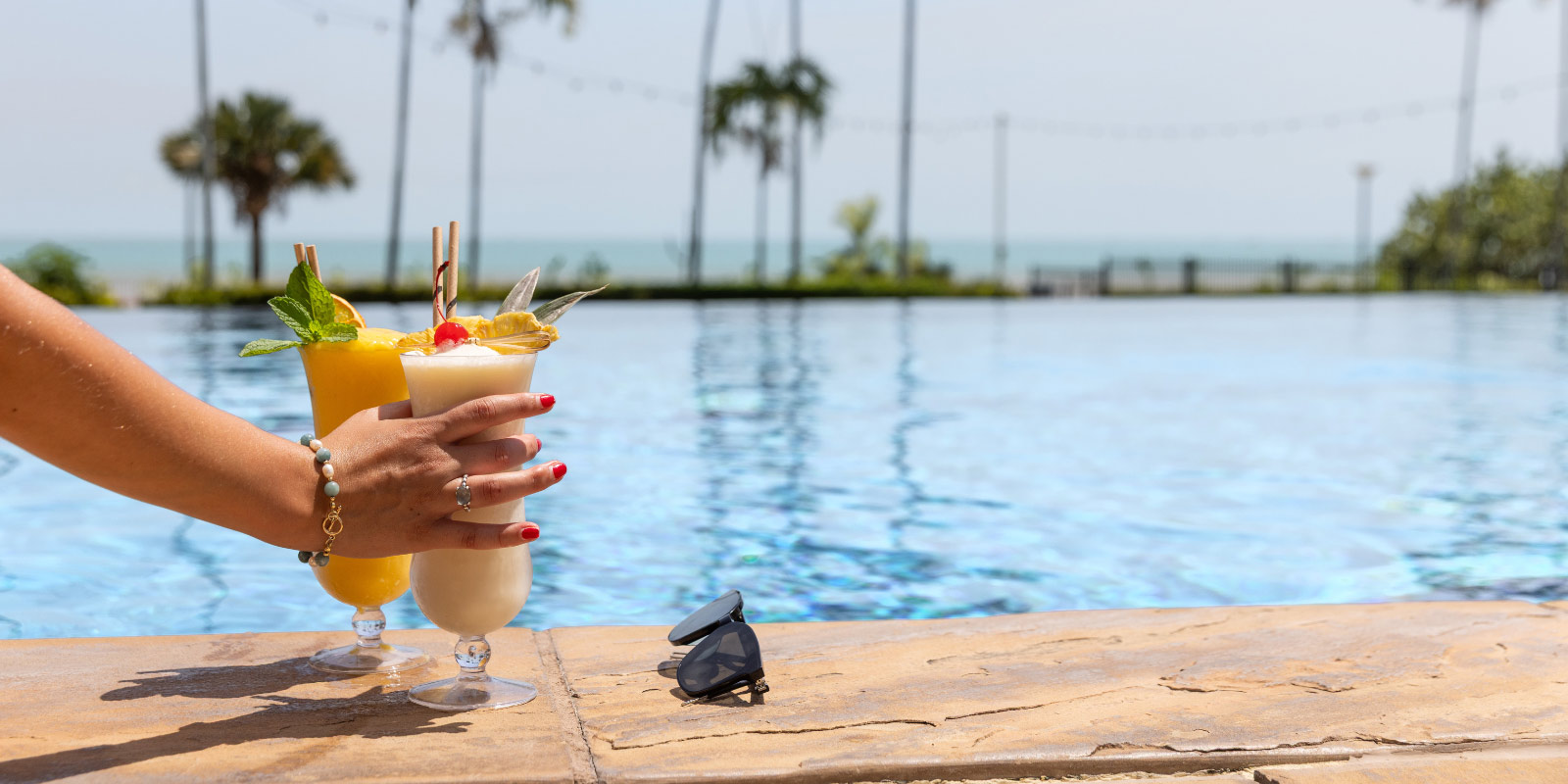 A hand grabbing a fruit drink at the edge of the pool.