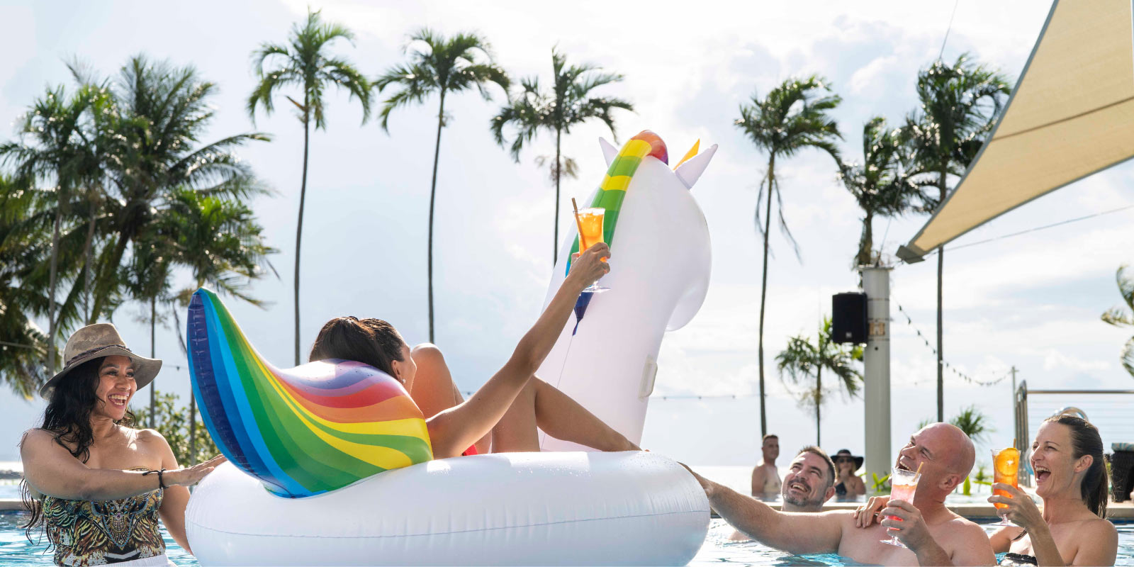 Group of people in the pool with a unicorn pool float and drinks.