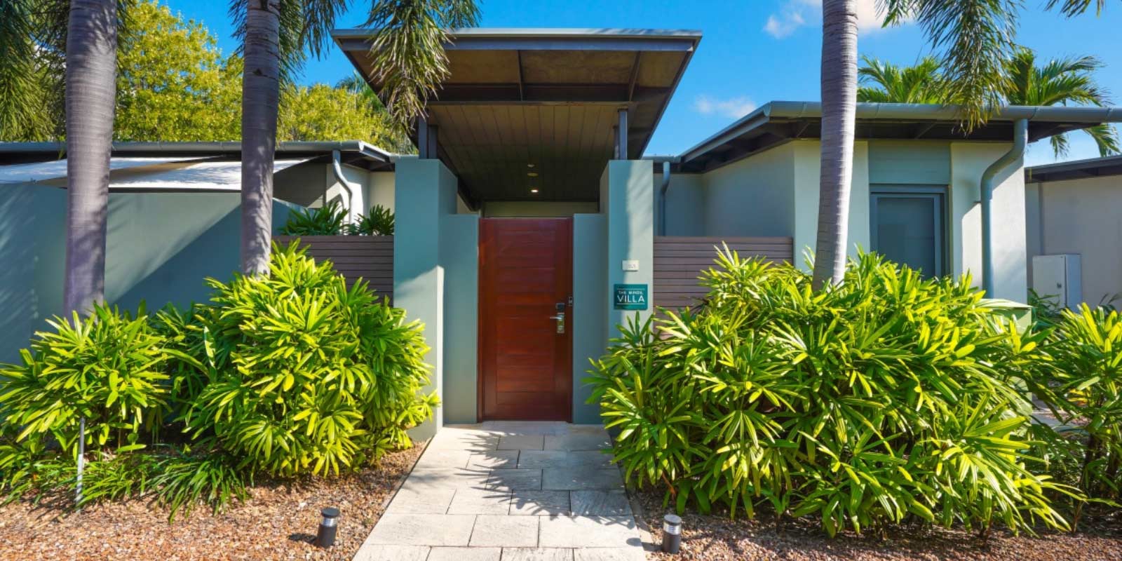 Exterior shot of the entrance way to the villa featuring native plants and palm trees.